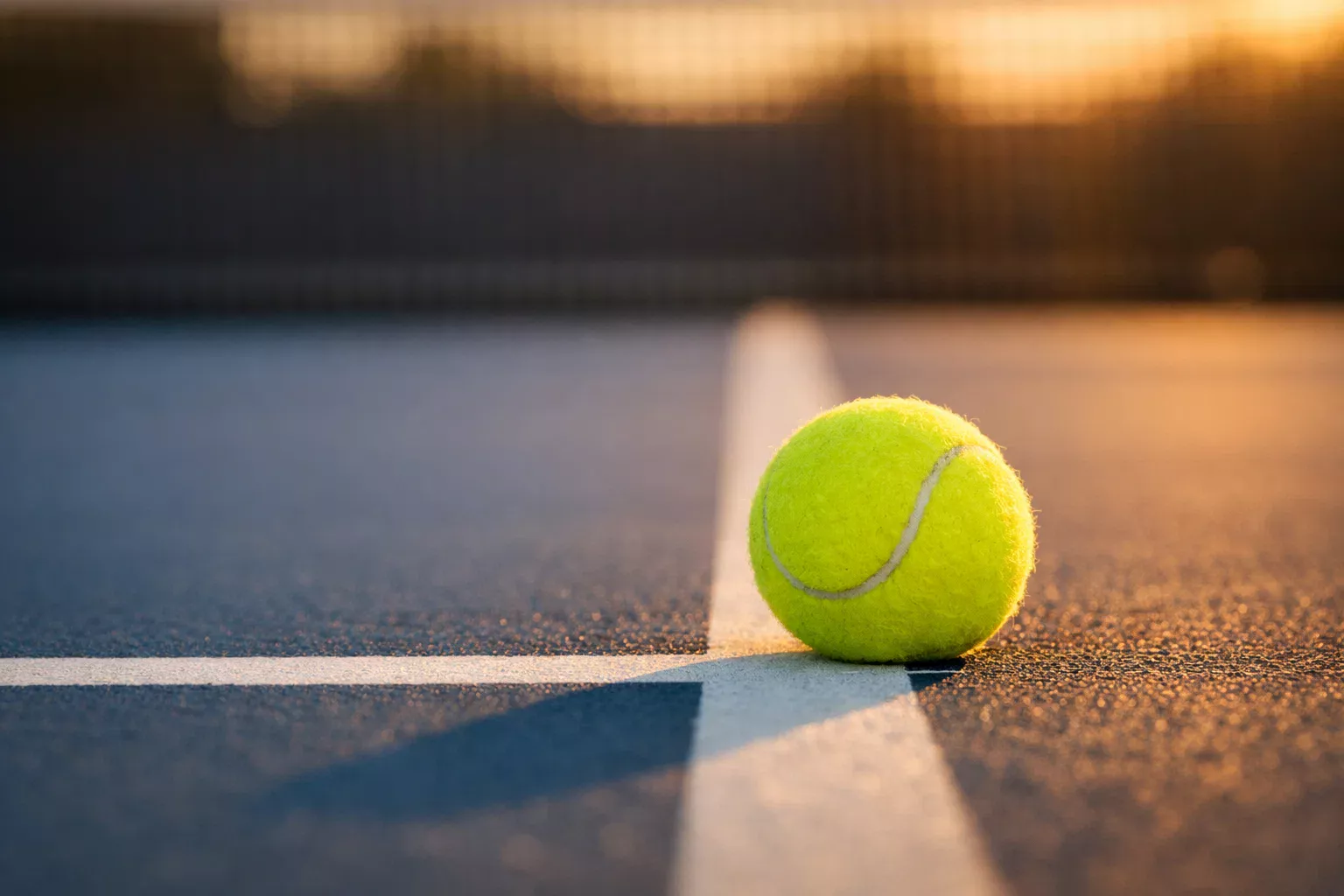 Tennisball auf der weissen Linie eines Tennisplatzes bei Sonnenuntergang